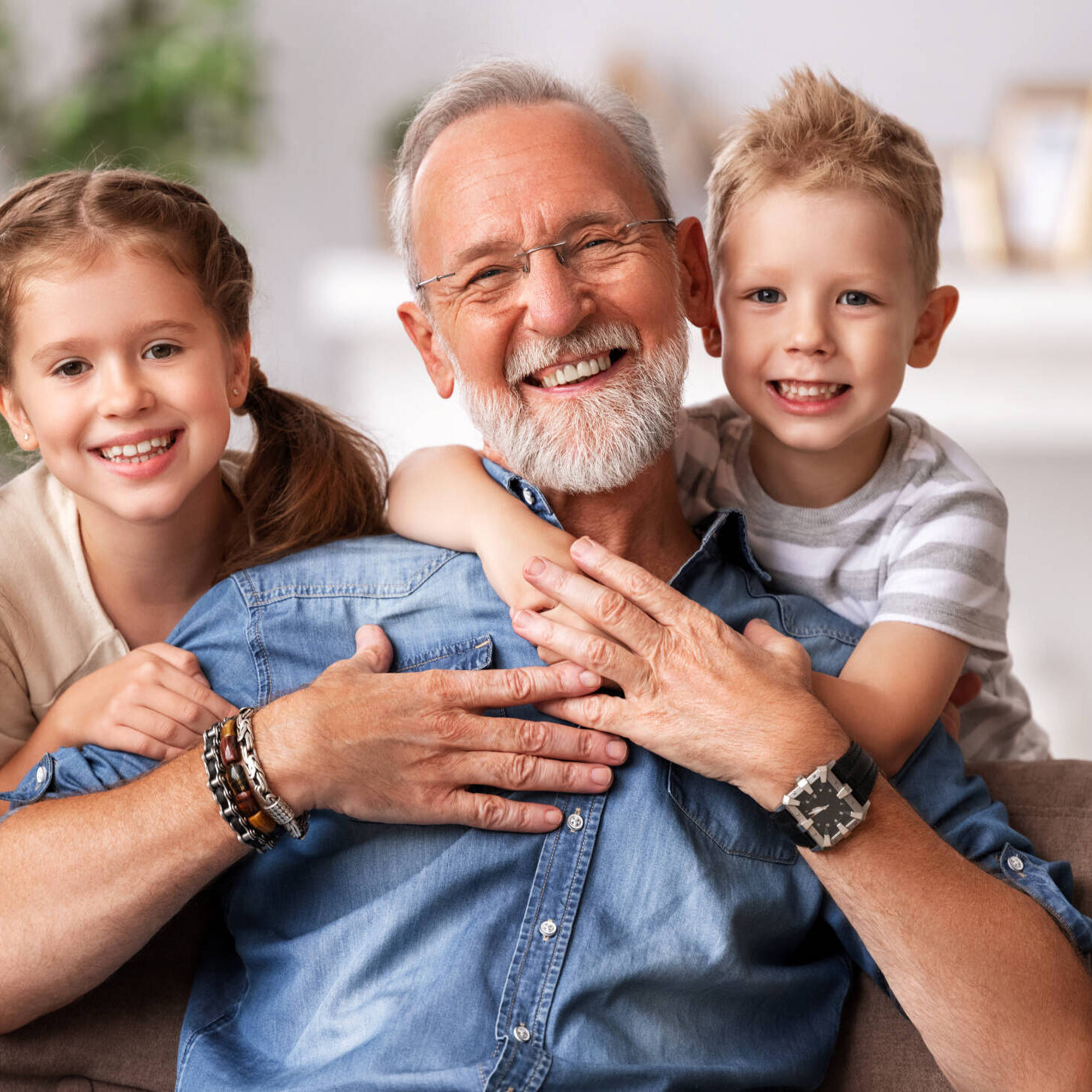 Happy family joyful little children hugging   grandfather   while sitting together on sofa and looking at camera on grandparents day